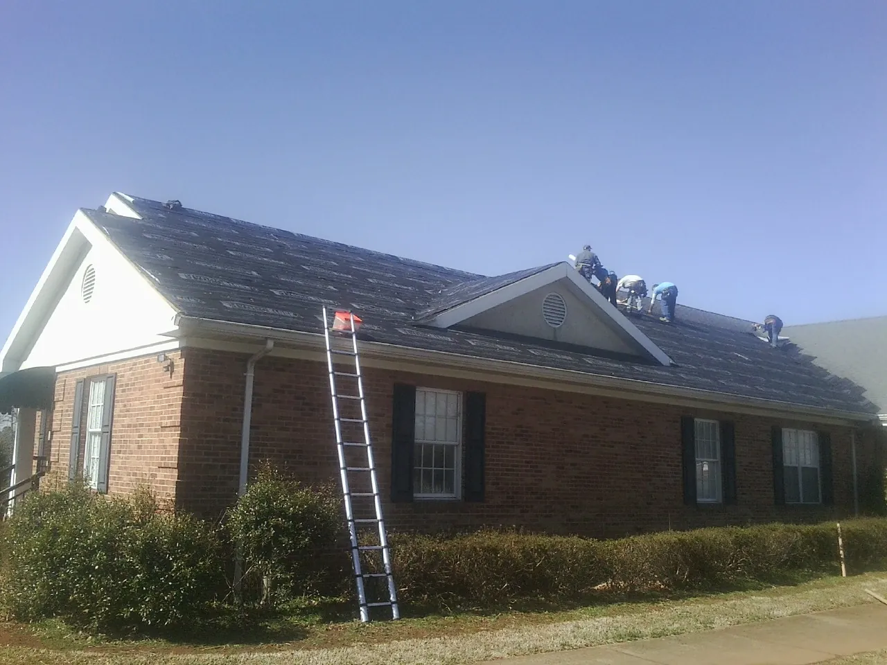 Crew tearing shingles off a brick ranch roof with a ladder set — Emergency Roof Repair work by our crew in Hilmar