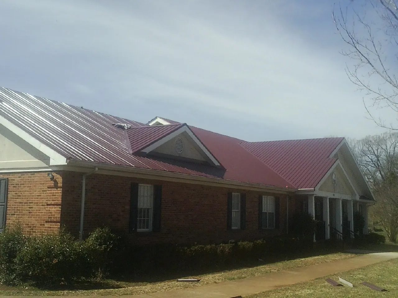 Red metal roof with gabled entries on a long brick building, from a Hail Damage Roof Repair job in Hilmar