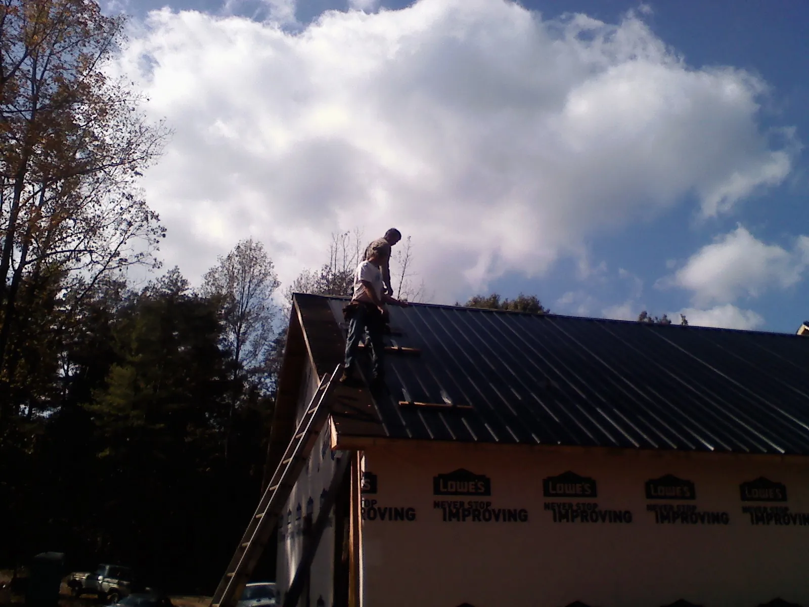 Roofer fastening dark metal panels high against a cloudy sky, from a Roof Inspection job in Hilmar